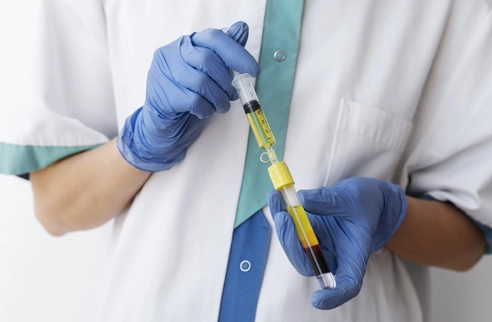 Lab technician wearing gloves handling syringe and vial with separated blood plasma sample